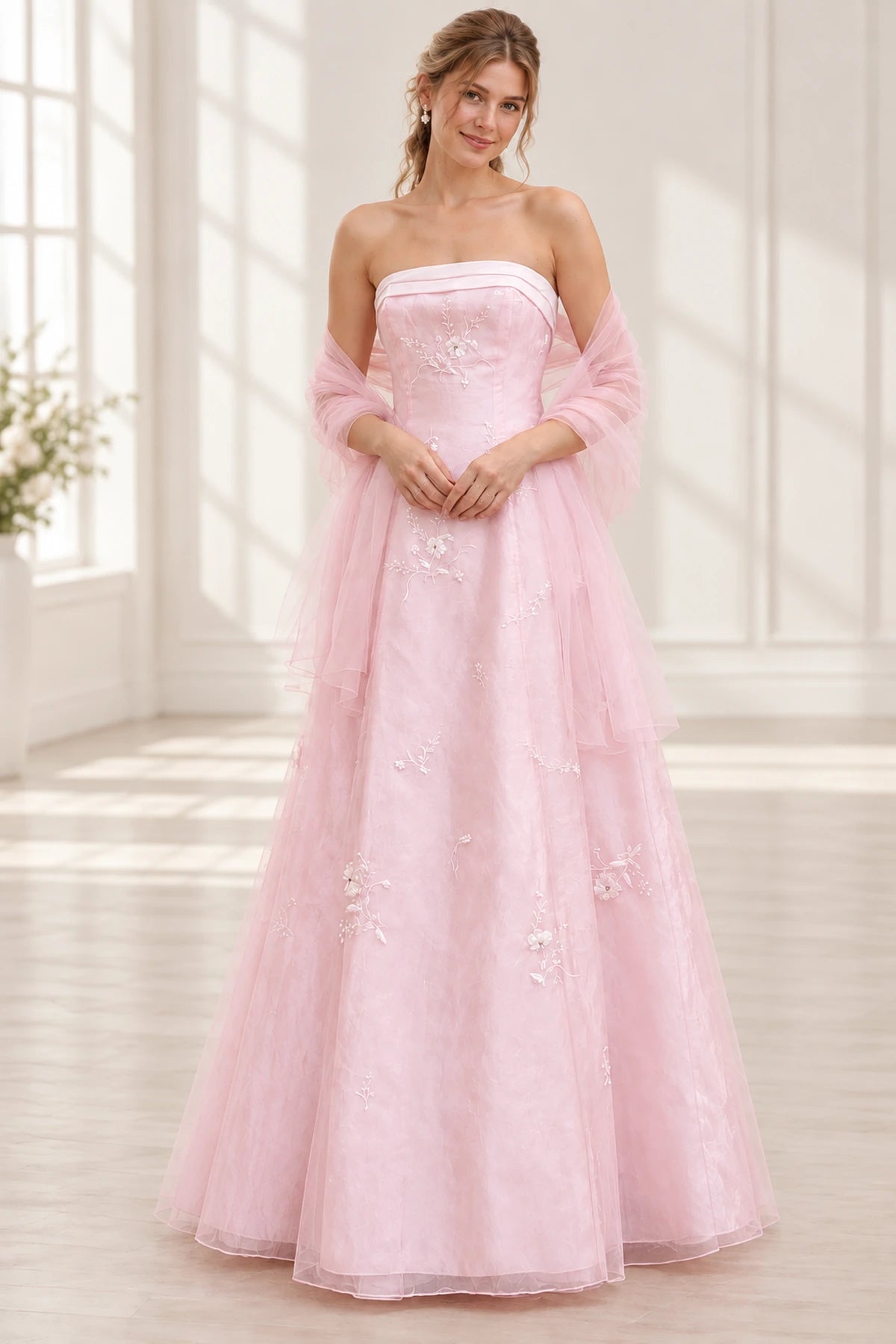 Blush pink floral tulle A-line prom dress front view featuring a strapless neckline, embroidered corset bodice, 3D floral appliques and flowing floor-length skirt