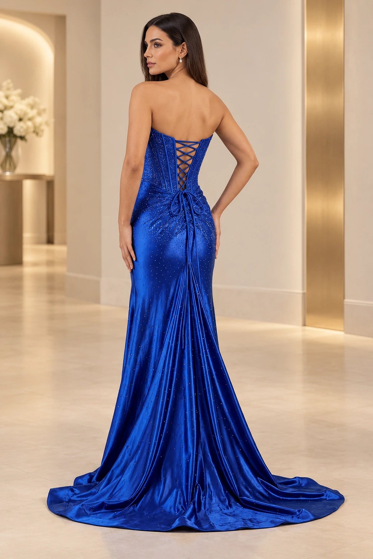 Royal blue prom dress with an exposed crisscross lace-up back, waist bow, center-back gathers, sparkling details, and sweeping train.