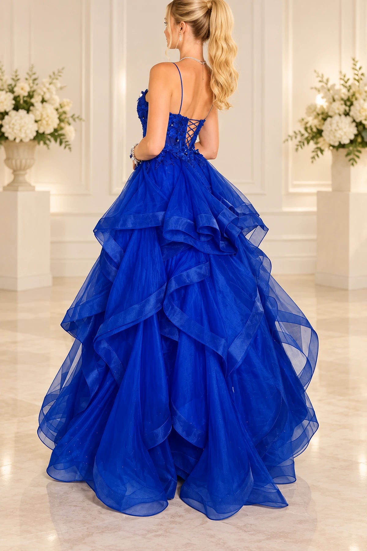 Back view of royal blue princess prom dress featuring delicate spaghetti straps, a lace-up corset back, floral appliques, and layered tulle ruffle skirt.