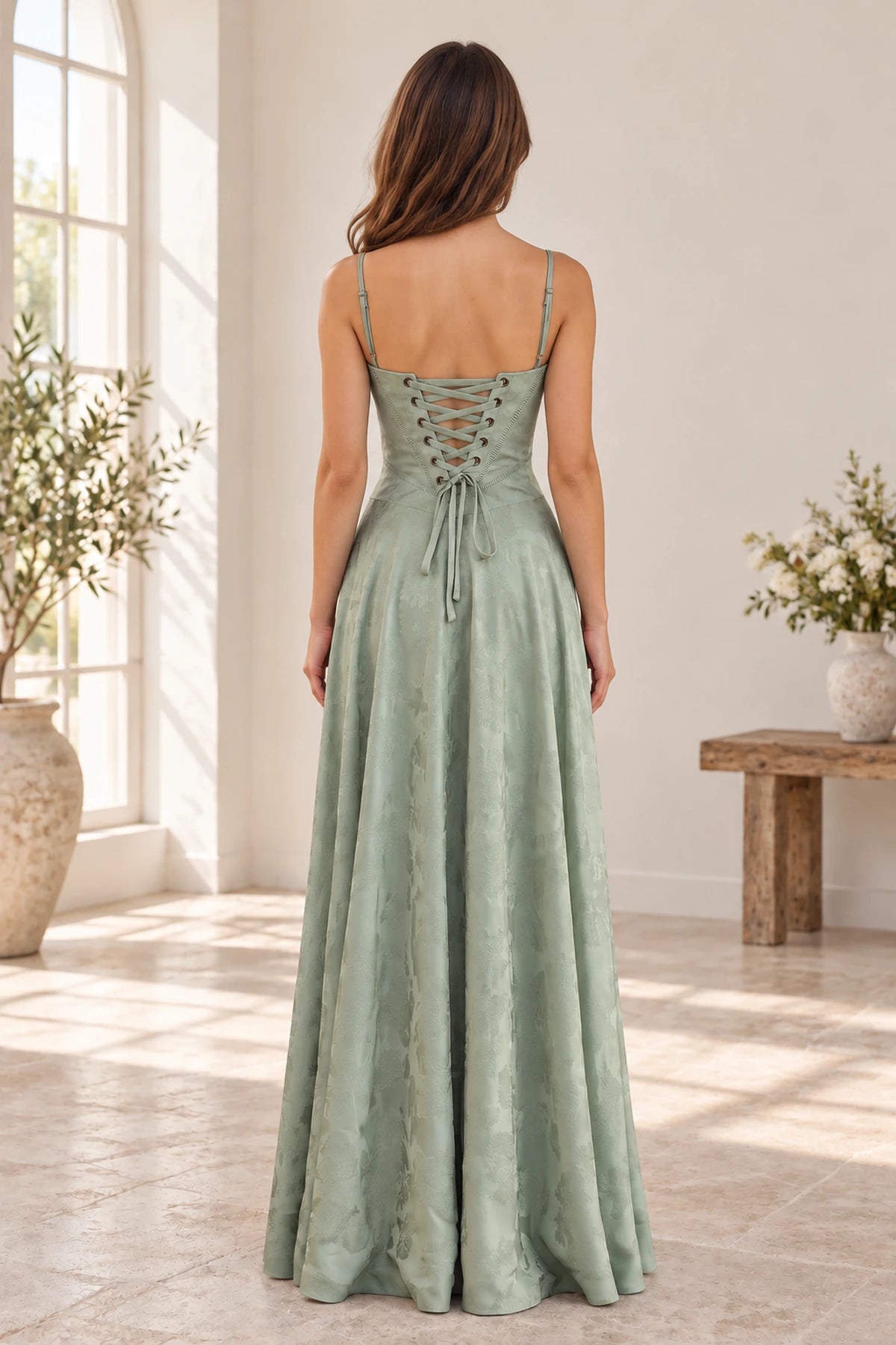 Back view of sage green floral jacquard prom dress featuring adjustable spaghetti straps, lace-up corset closure and flowing A-line skirt.