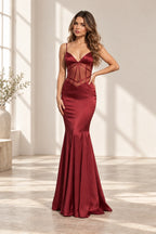 Burgundy satin mermaid prom dress with plunging V neckline, spaghetti straps, sheer corset waist and fitted floor length flared skirt by Graceprom