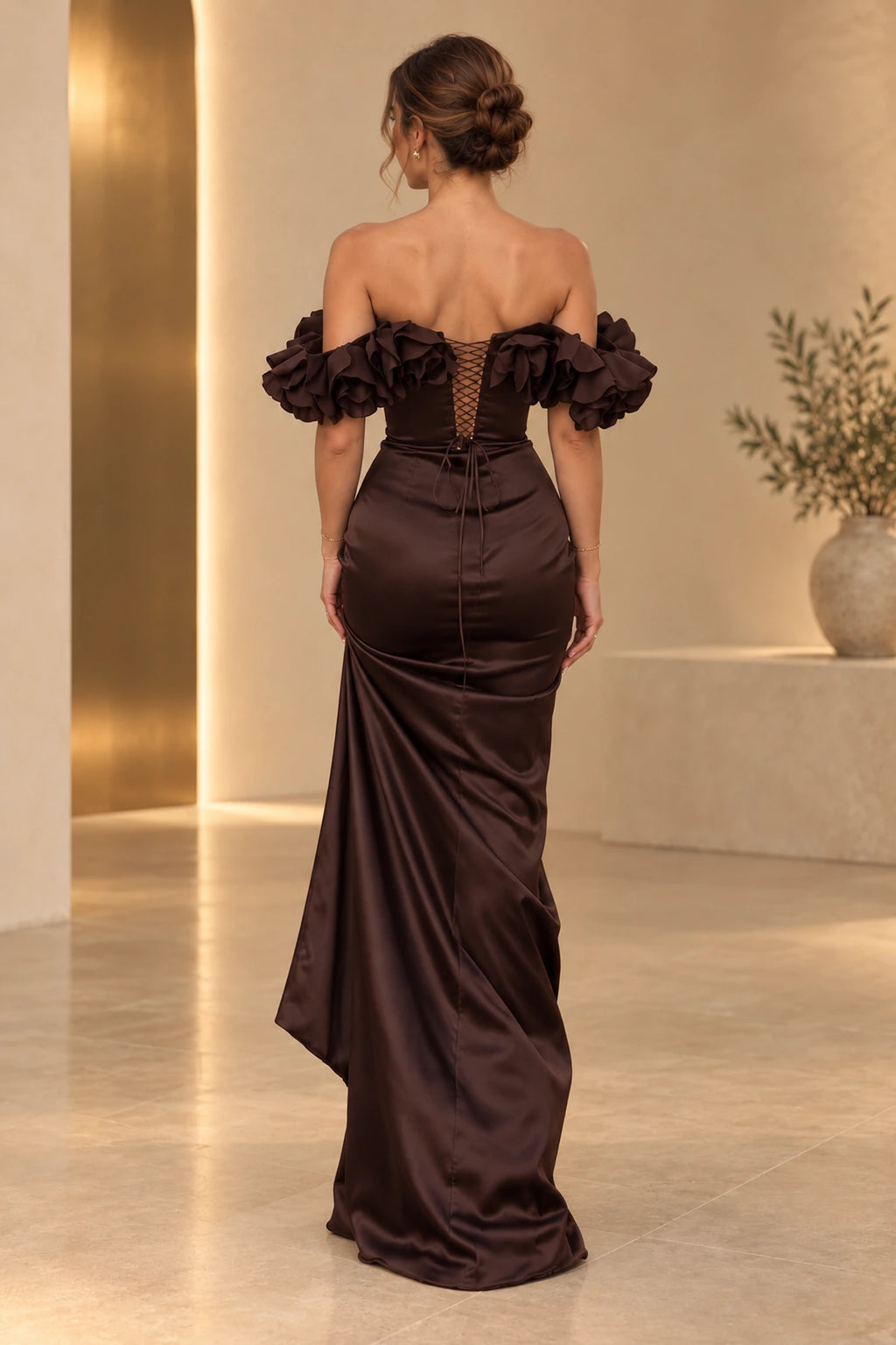 Back view of chocolate brown satin mermaid evening dress featuring off shoulder ruffle sleeves, lace up corset back and flowing floor length skirt