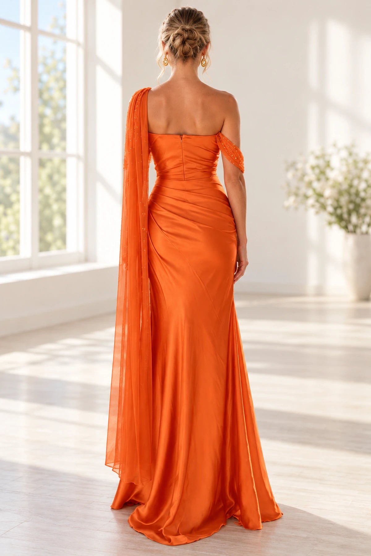 Back view of an orange Graceprom satin prom dress with a straight back neckline, center zipper, ruched hips and a long sheer shoulder drape.
