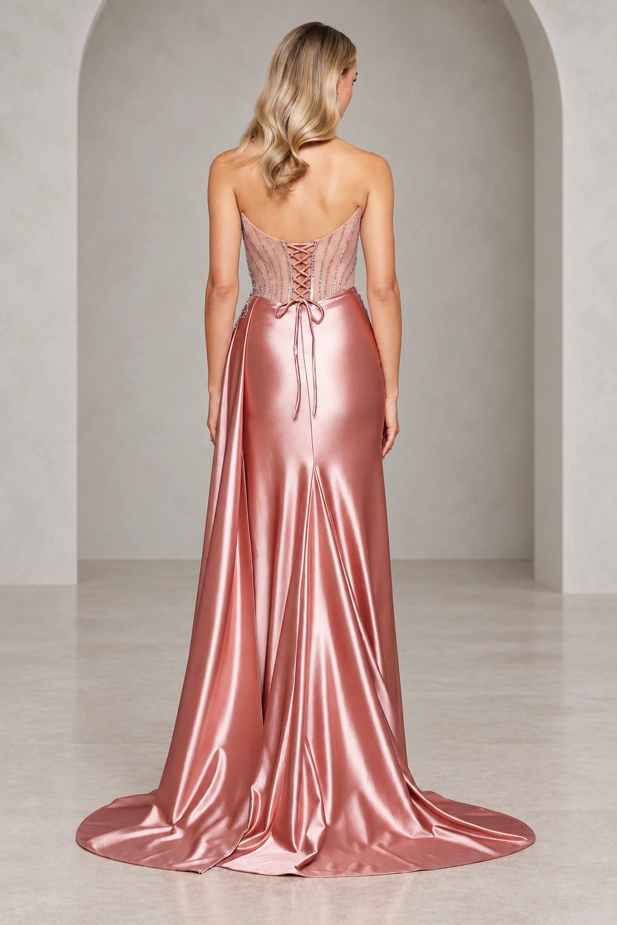 Back view of a rose prom dress with a low curved neckline, sheer beaded panels, crisscross waist ties, and a softly flared skirt with a short train.