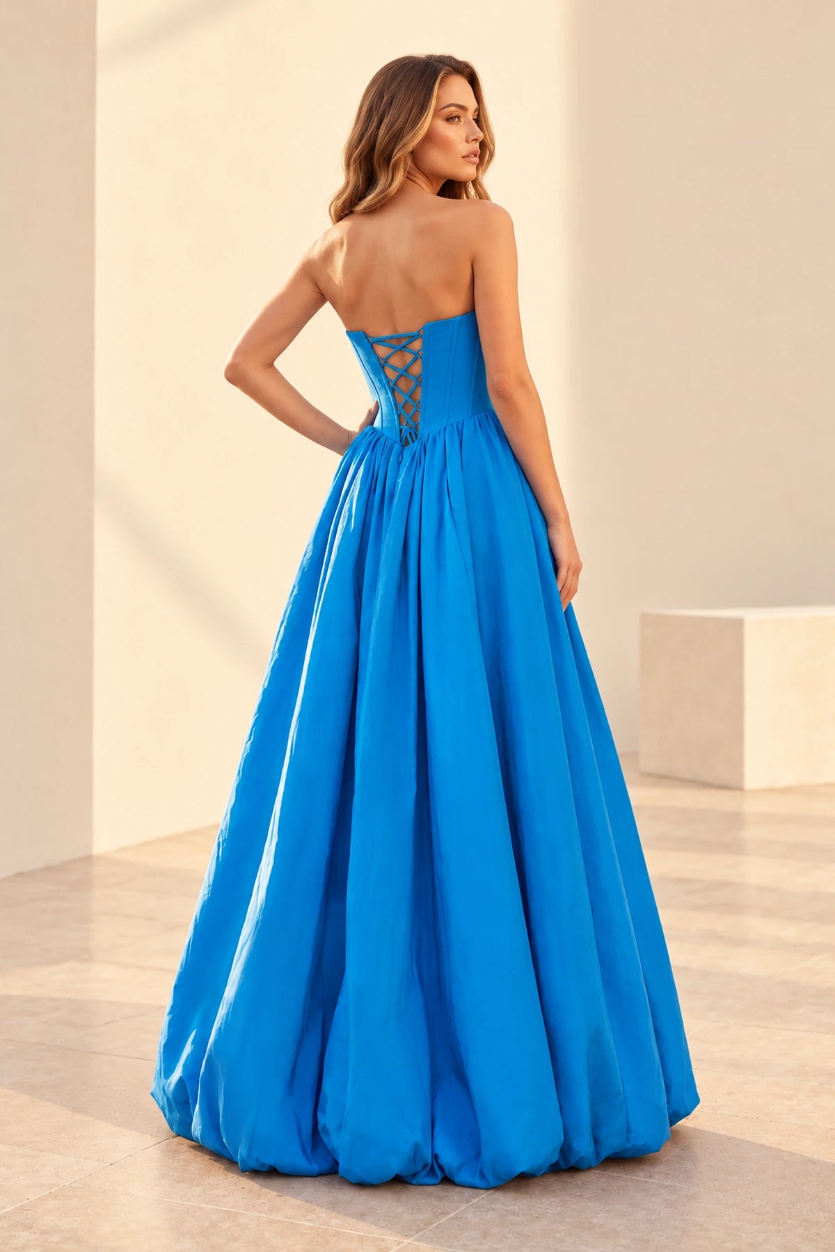 Back view of a blue prom dress with a low crisscross lace-up bodice and a full gathered floor-length skirt with a rounded bubble hem.