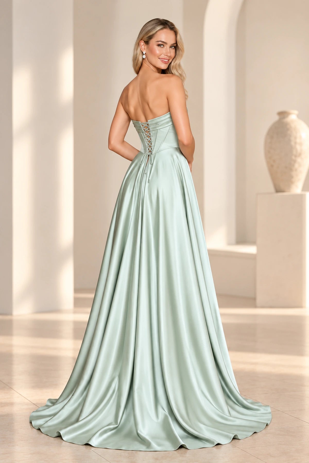 Back view of a sage green satin prom dress with a low lace-up corset back, folded neckline band, flowing A-line skirt, and short train.