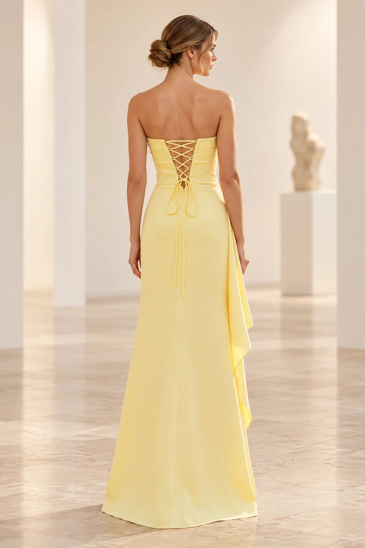 Back view of butter yellow strapless prom dress featuring a crisscross lace-up corset closure, fitted waist and flowing floor-length sheath skirt.