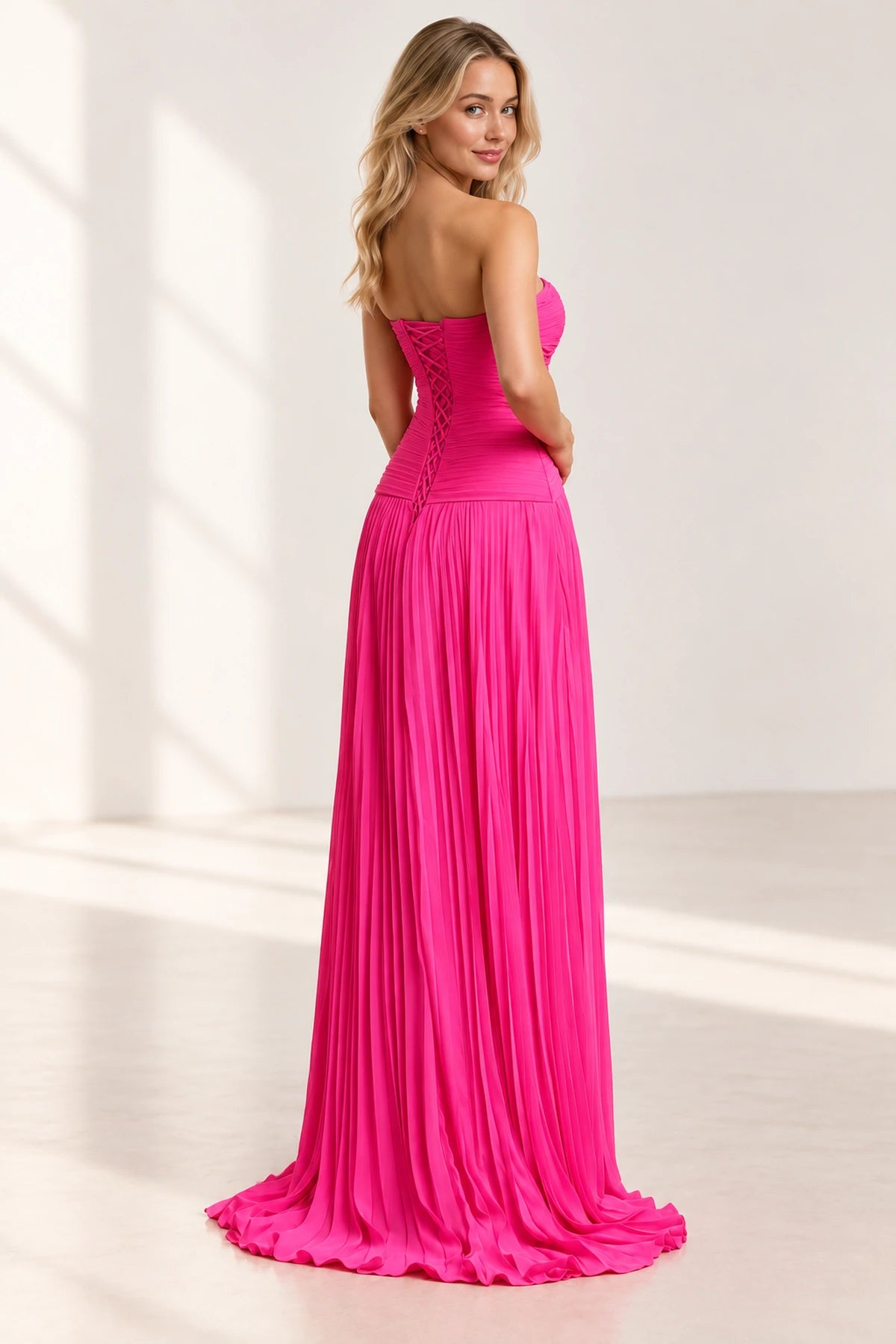 Back view of hot pink strapless A-line prom dress featuring a lace-up corset closure, ruched fitted bodice and flowing pleated skirt.