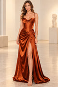 Rust satin prom dress with a draped sweetheart neckline, spaghetti straps, corset-style bodice, gathered hip detail, and thigh-high slit.