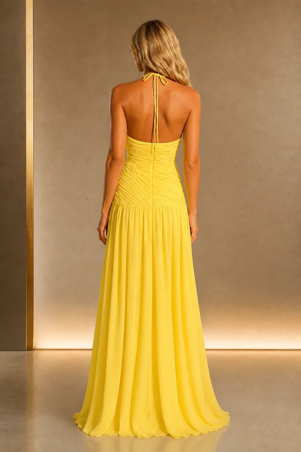 Back view of yellow wedding guest dress with halter tie, open back, ruched bodice and flowing floor-length A-line skirt